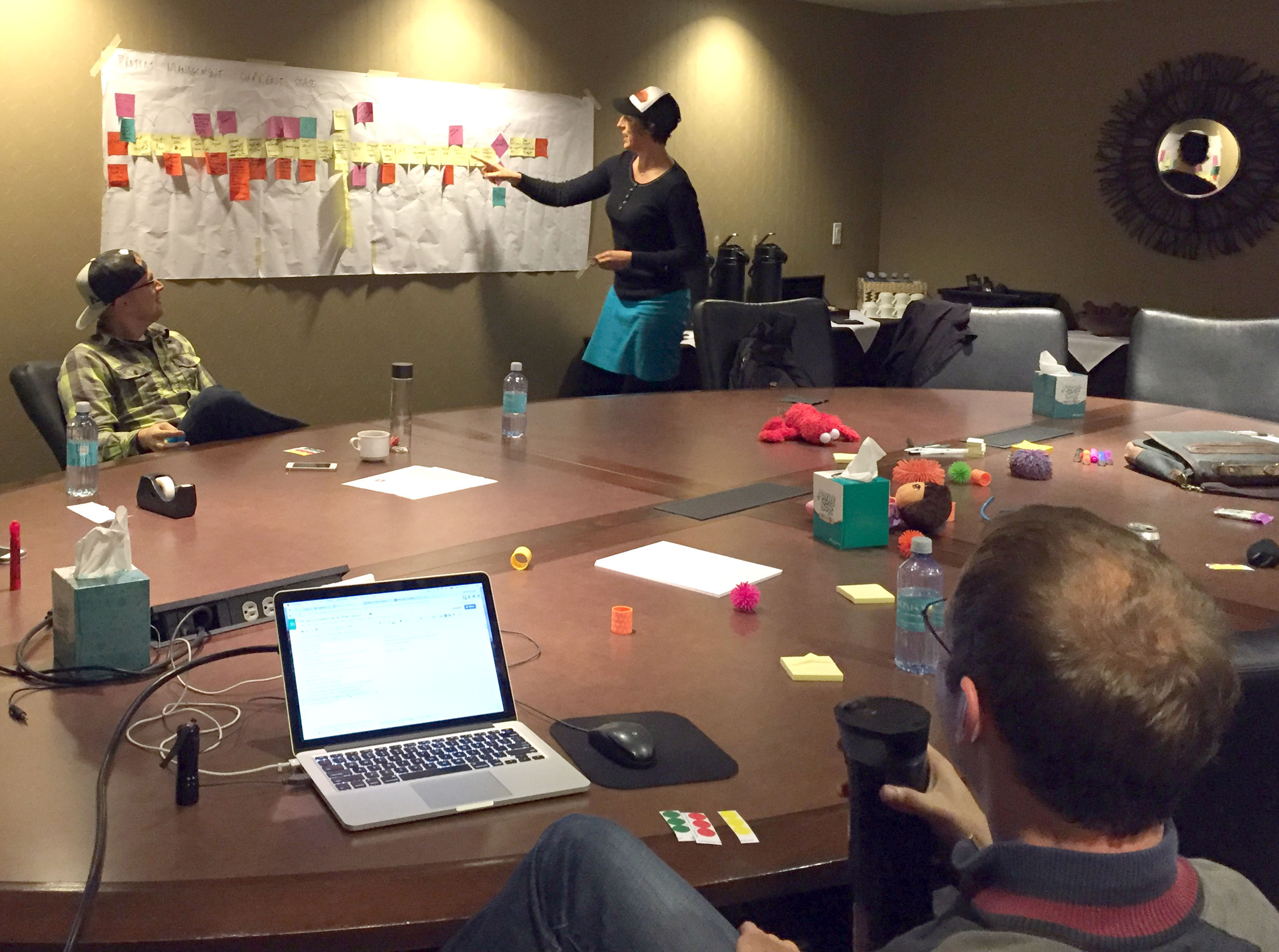 2 people sitting around a conference table with 1 person standing at the wall facilitating